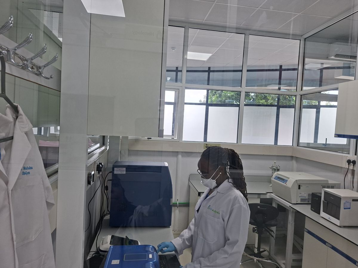 CA Medlynks lab technician in full PPE processing samples behind biosafety glass