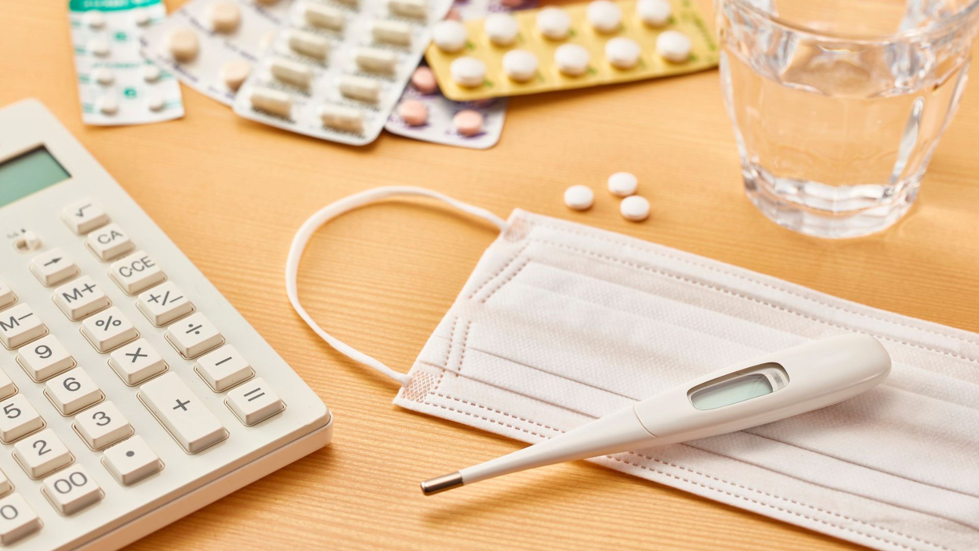 Blister packs of tablets, a thermometer and a glass of water on a table, representing treatment for a diagnosed infection
